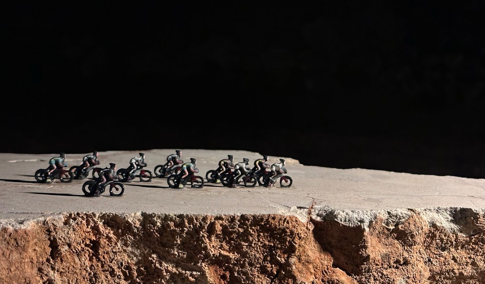 Un gruppo di ciclisti in miniatura in volata su una pietra, di notte