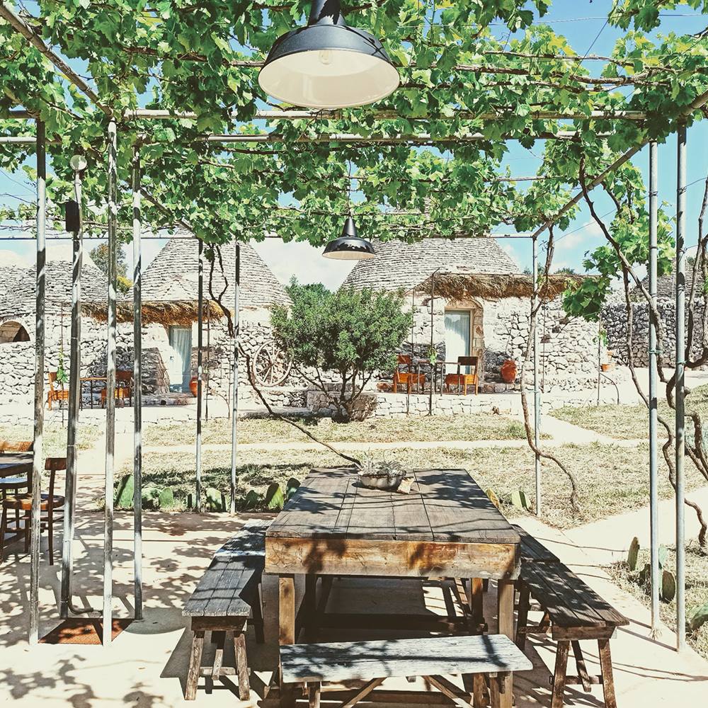 La tavola lunga sotto il pergolato, davanti ai trulli